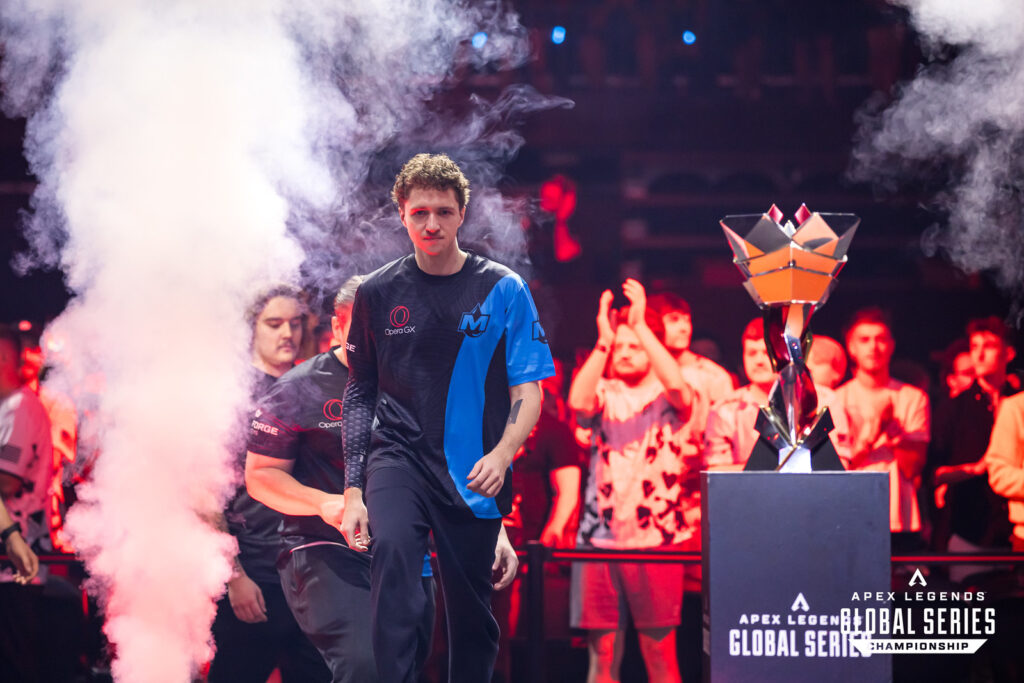 A professional esports player walks onto the stage at the Apex Legends Global Series Championship, with the Championship trophy to the right of the photo. 